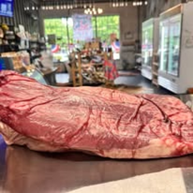A whole fresh cut of beef resting on the butcher case